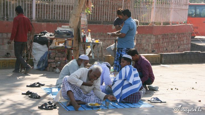 Egy csapat indiai férfi eszik egy leterített lepedőn a parkoló szélén