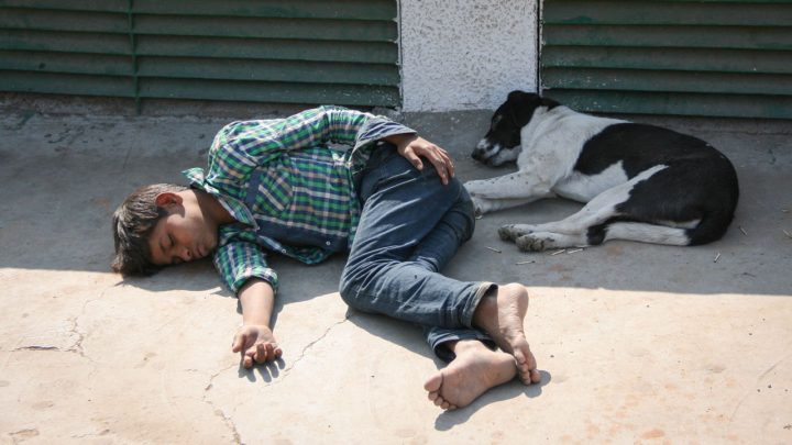 8-10 éves indiai fiú alszik mezitláb egy kutya mellett a földön