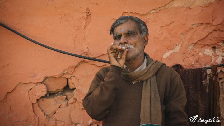 Férfi áll egy színes fal előtt, miközben cigarettáját szívja