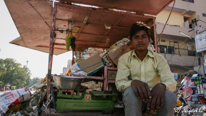 Fiatal indiai fiú ül a gyümölcs árusító kocsiján a kamerába nézve