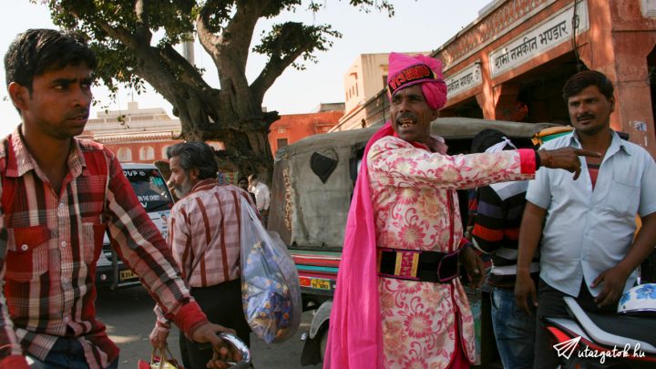 egy rózsaszín palástot ruhába öltözött indiai férfi mutogat az egyik utcasrakon