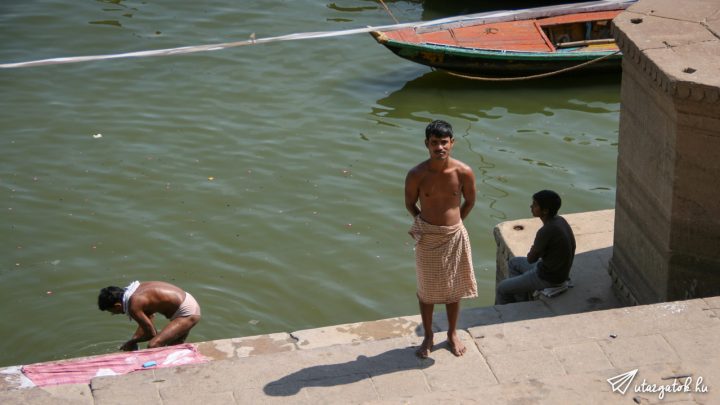 Fiatal indiai férfi áll vigyázba félmeztelenül egy törölközővel a derekán a kamerába nézve a Gangesz partján fürdés után