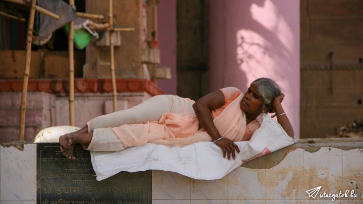 egy indiai nő fekszik úgy az oldalán, mintha csak otthon nézne TV-t a nyilt utcán