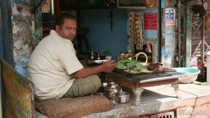 Indiai férfi törökülésben boltjában kinn az utcafronton