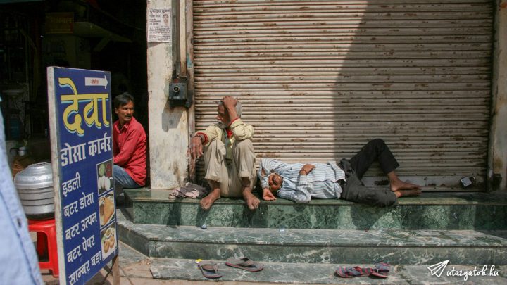 Indiai férfiak pihennek egy bolt lépcsőjén, egyikük alszik